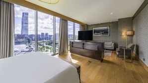 Une chambre d’hôtel moderne dotée d’un grand lit, d’une télévision, d’un canapé et d’un bureau. La chambre dispose de grandes fenêtres offrant une vue sur la ville.