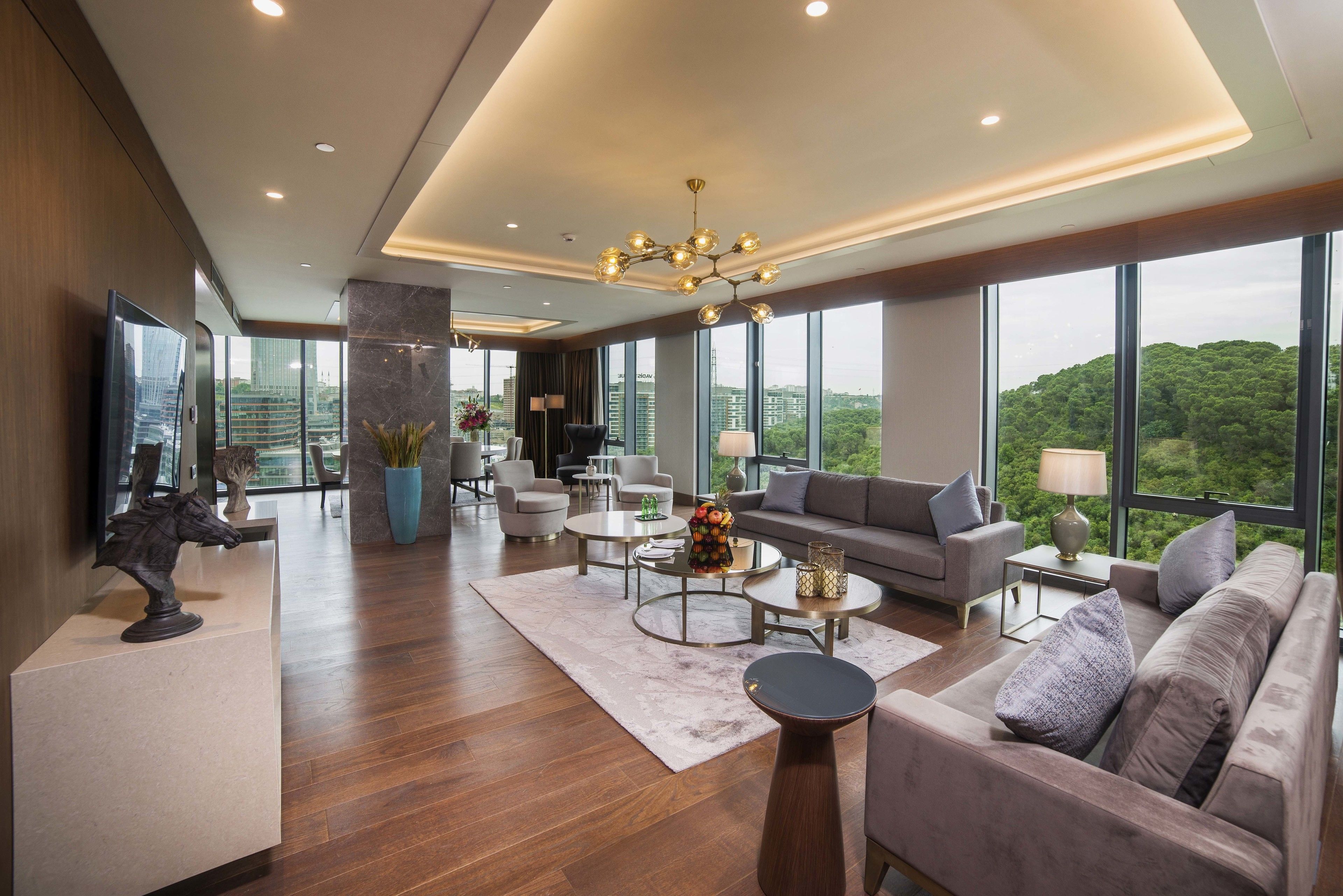 Amplia sala de estar con una lámpara moderna, ventanas grandes con vistas a la ciudad y un cómodo espacio para sentarse.
