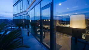 Un bâtiment moderne doté de grandes fenêtres en verre, d’une terrasse et d’un intérieur bien éclairé.