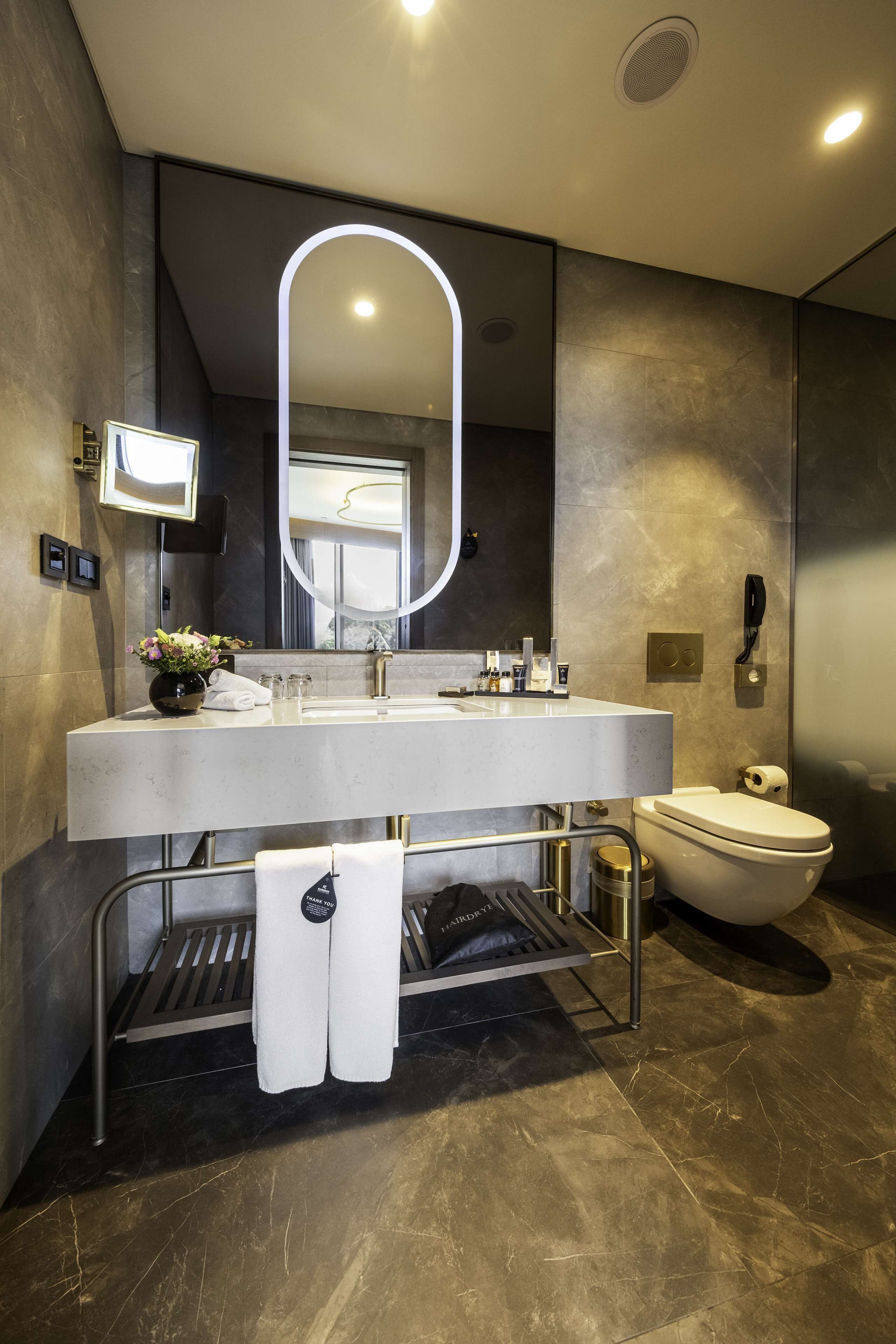 A modern bathroom with a large mirror, a sink, and a toilet.