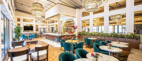 Un amplio vestíbulo de hotel con techos altos, varias zonas de estar y un bar.