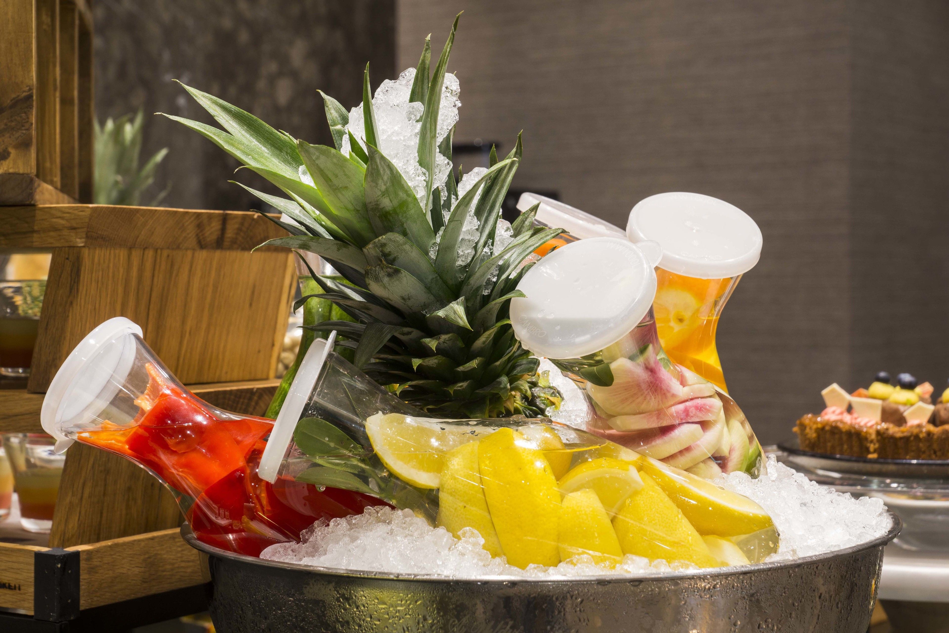 A beverage dispenser with a pineapple, lemons, and a bottle of red drink on ice.