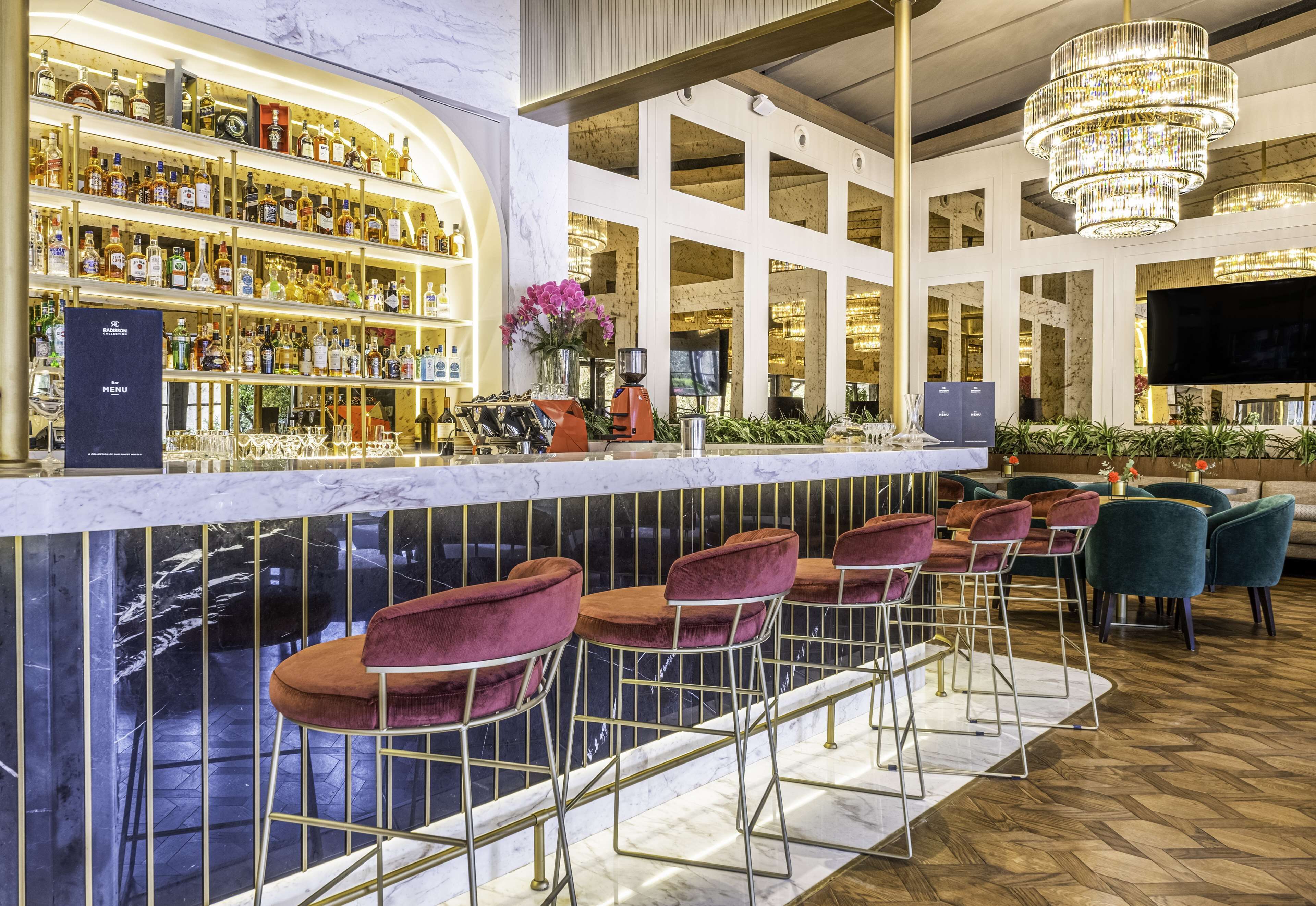 Una zona de bar con mostrador de mármol, varios taburetes y una amplia variedad de botellas de licor.
