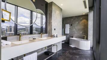 Ein modernes Badezimmer mit einem großzügigen Waschtisch, einer freistehenden Badewanne und Blick auf die Stadt durch bodengrosse Fenster.