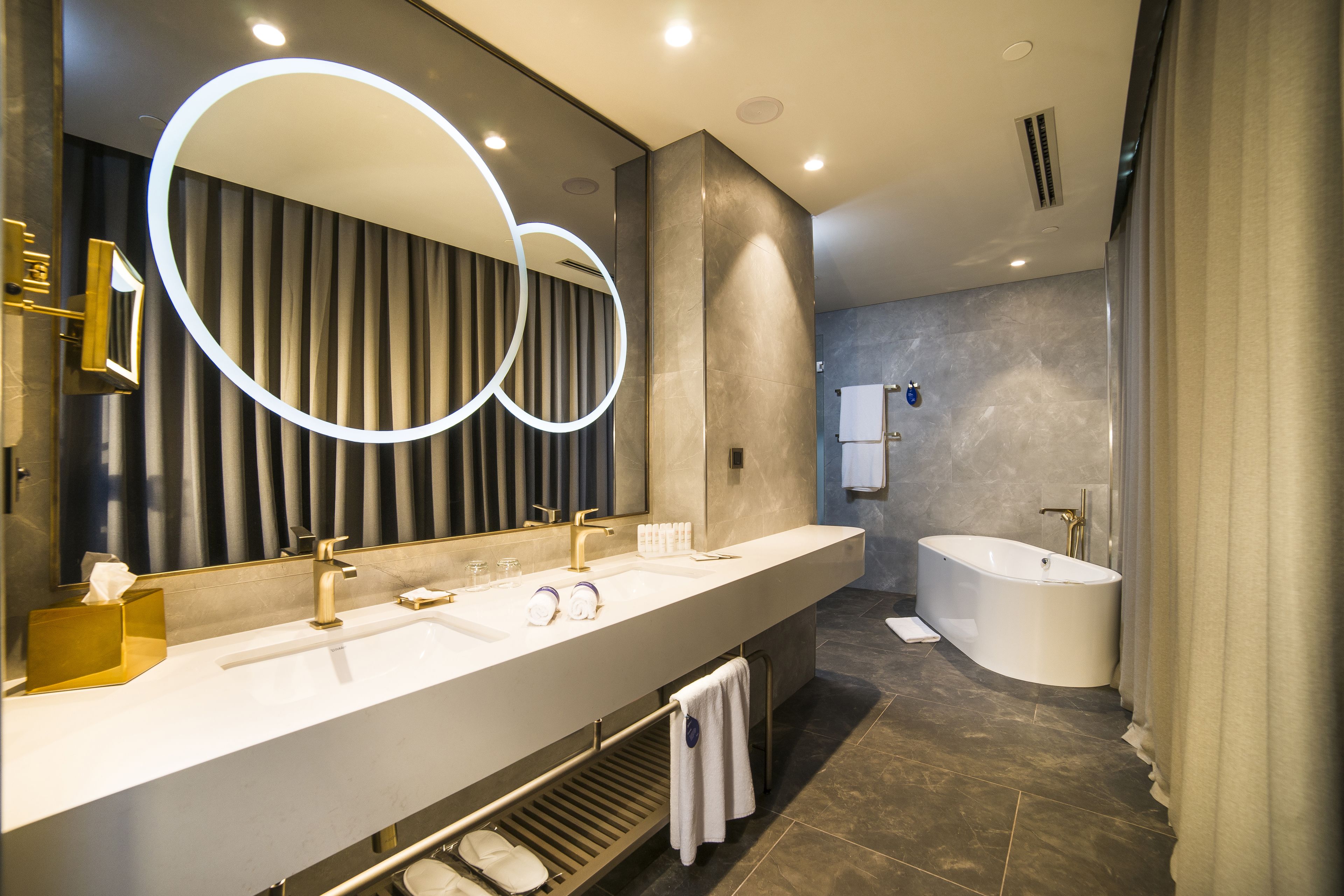 A modern bathroom with a large mirror, two sinks, a bathtub, and a towel rack.
