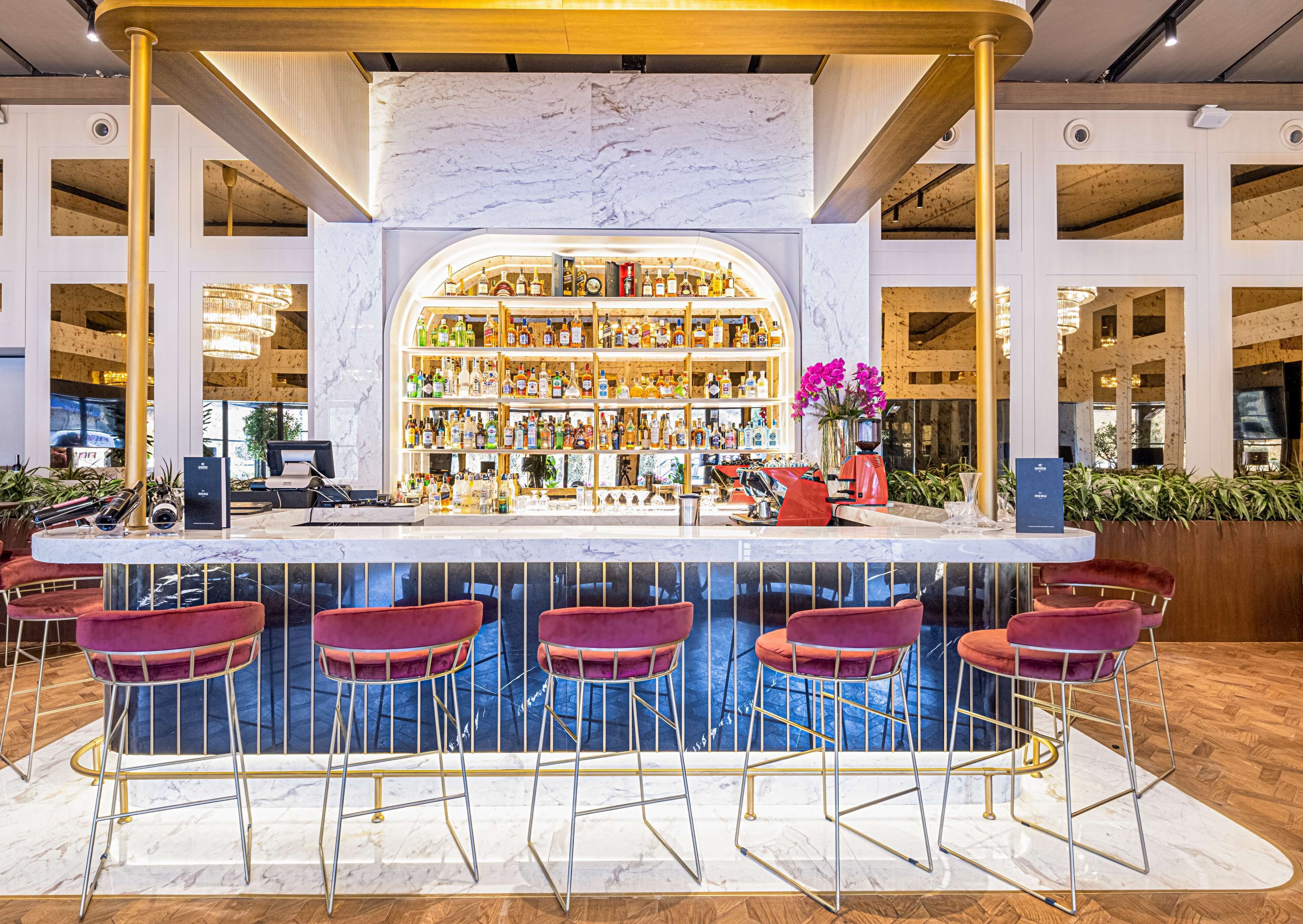 Un espace bar doté d’un comptoir en marbre, de plusieurs tabourets et d’une variété de bouteilles d’alcool.