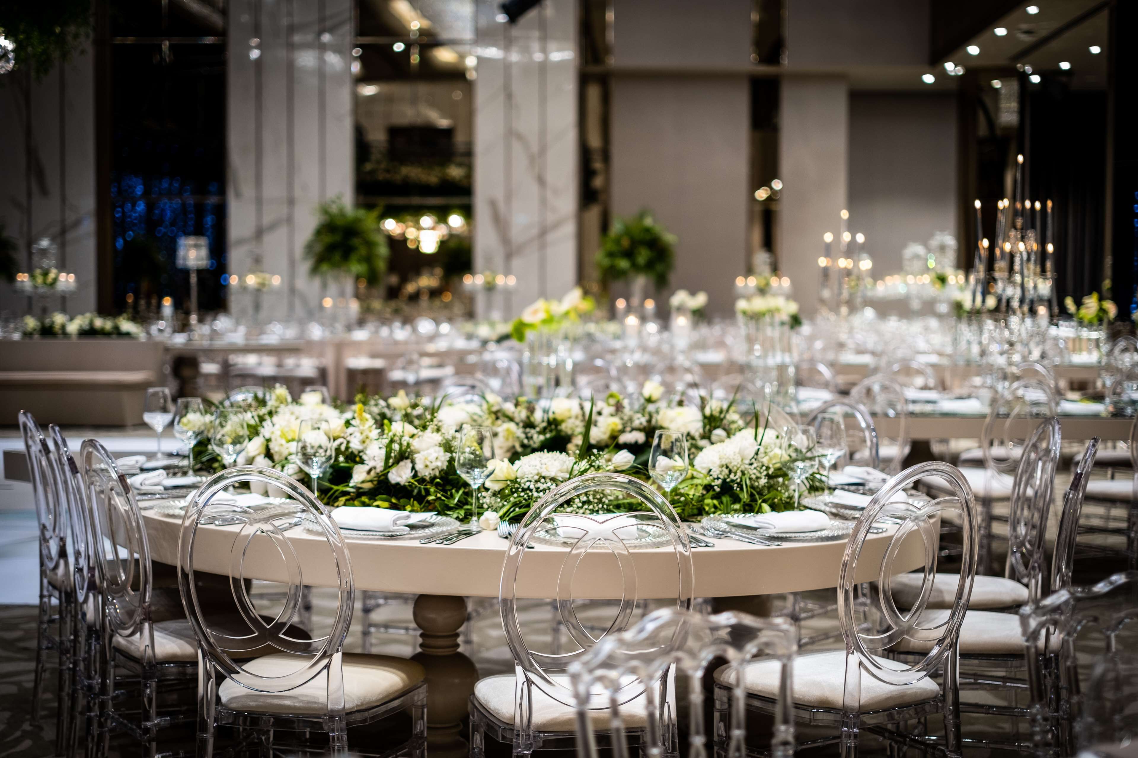 Escena formal de menjador amb taules rodones, caires transparents i centrals florals.