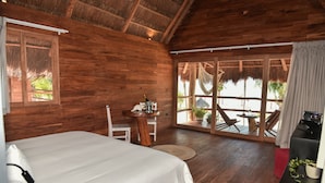 A wooden room with a bed, a table with a bottle, and a view of the beach.