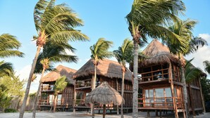 A beachfront resort with thatched-roof bungalows, palm trees, and a sandy beach.