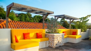An outdoor seating area with yellow cushions and a stone table, surrounded by a white wall and a wooden pergola. - 3 bdrm Town House at Runaway Bay (Runaway Bay)
