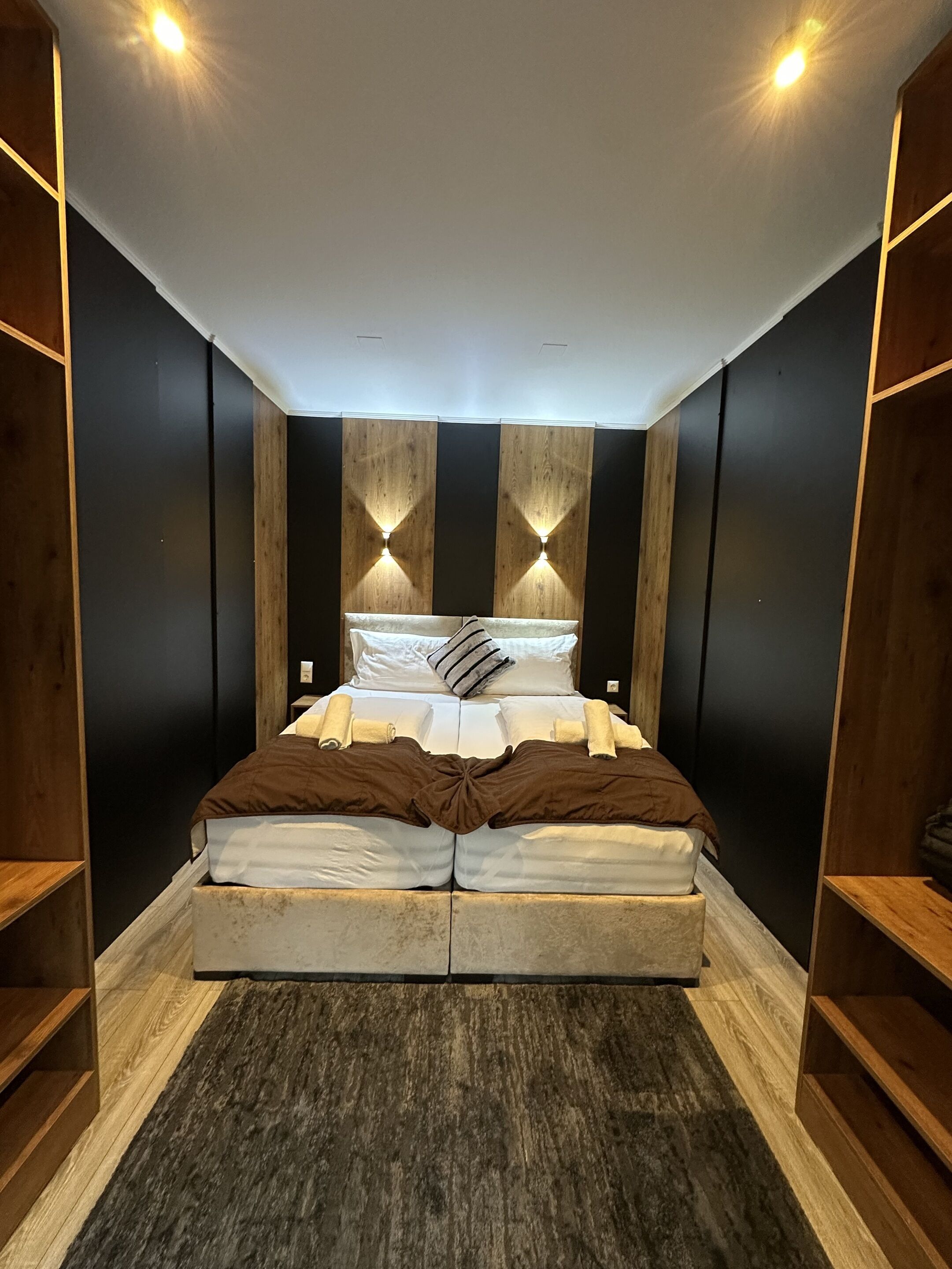 A modern bedroom with a large bed, wooden panel walls, and built-in lighting.