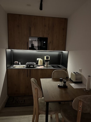A compact kitchen with a built-in oven, a coffee maker, and a toaster. There is a wooden dining table with chairs. - Apartmenthaus Zeuthen (Zeuthen)