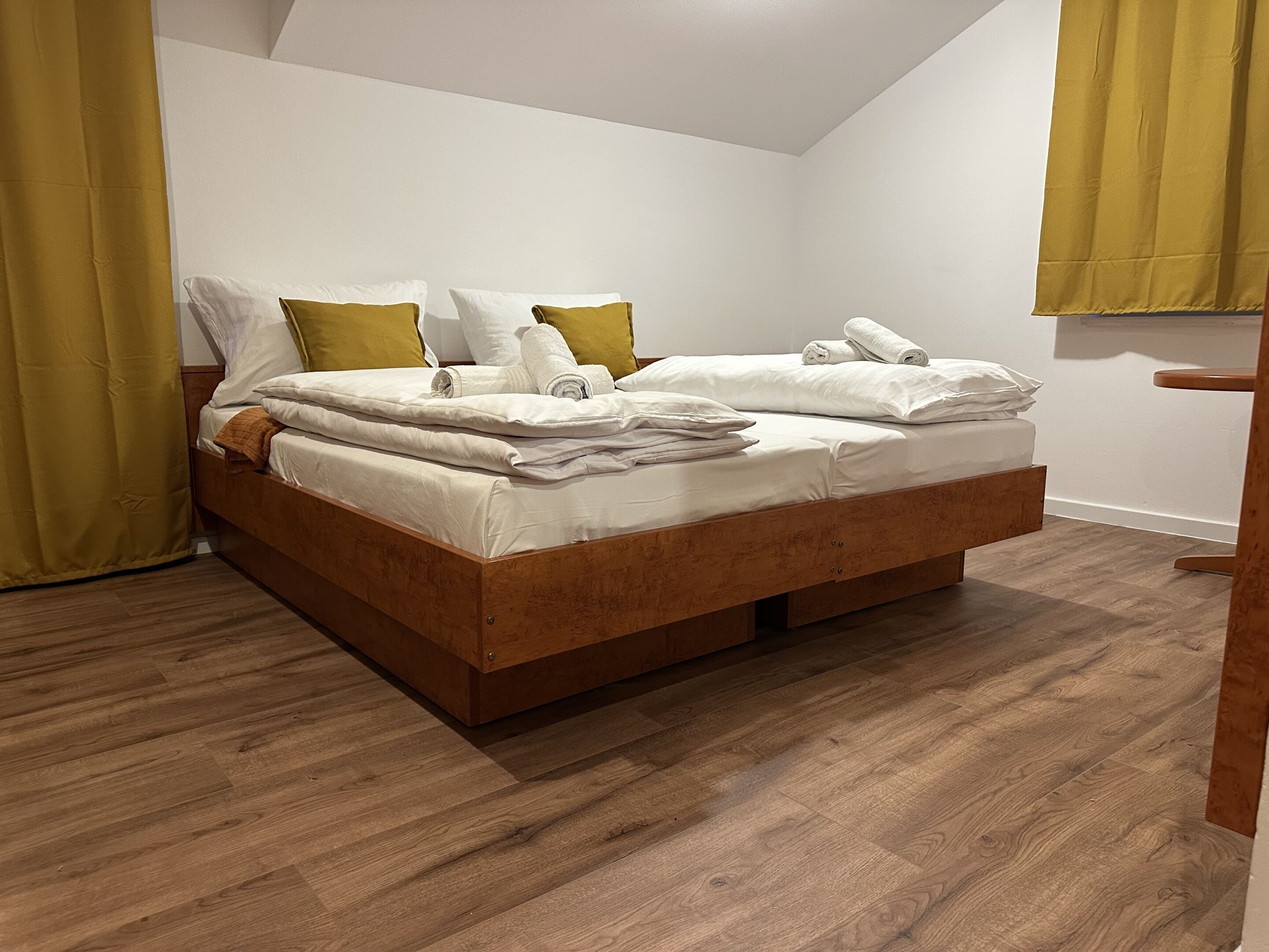 Un lit bien fait, avec une literie blanche et deux oreillers, une tête de lit en bois et un plancher en bois.