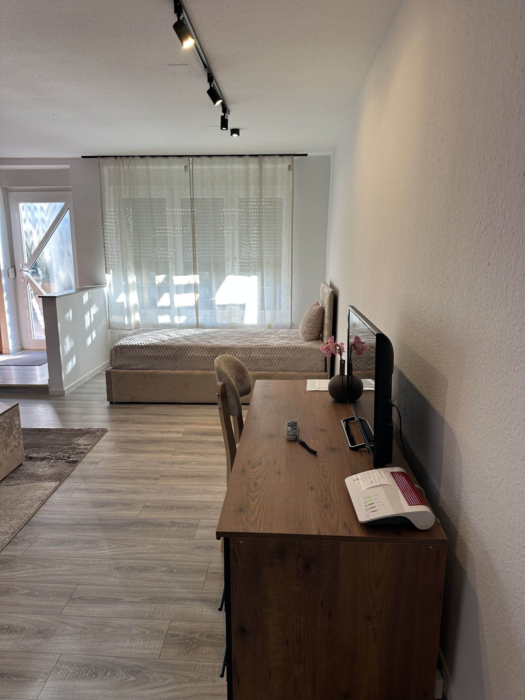 Una habitación moderna con un escritorio de madera, una cama con vistas y un ventanal con cortinas de gasa.