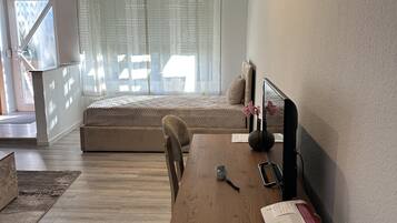 Una habitación moderna con un escritorio de madera, una cama con vistas y un ventanal con cortinas de gasa.