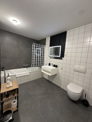 A modern bathroom with a bathtub, toilet, vanity, and a mirror. - Apartmenthaus Zeuthen (Zeuthen)