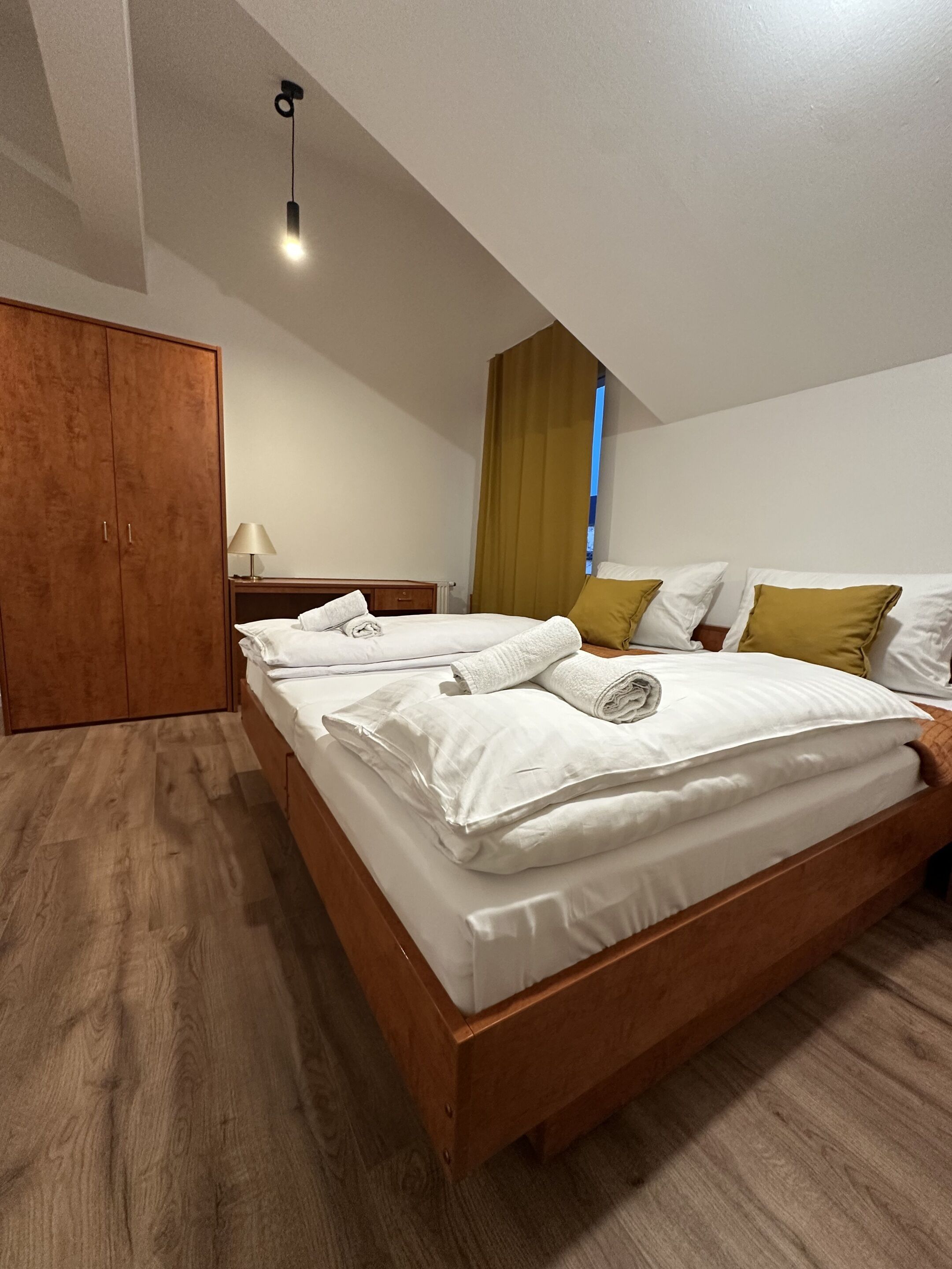 A bedroom with a wooden bed, a wardrobe, a nightstand, and a lamp.