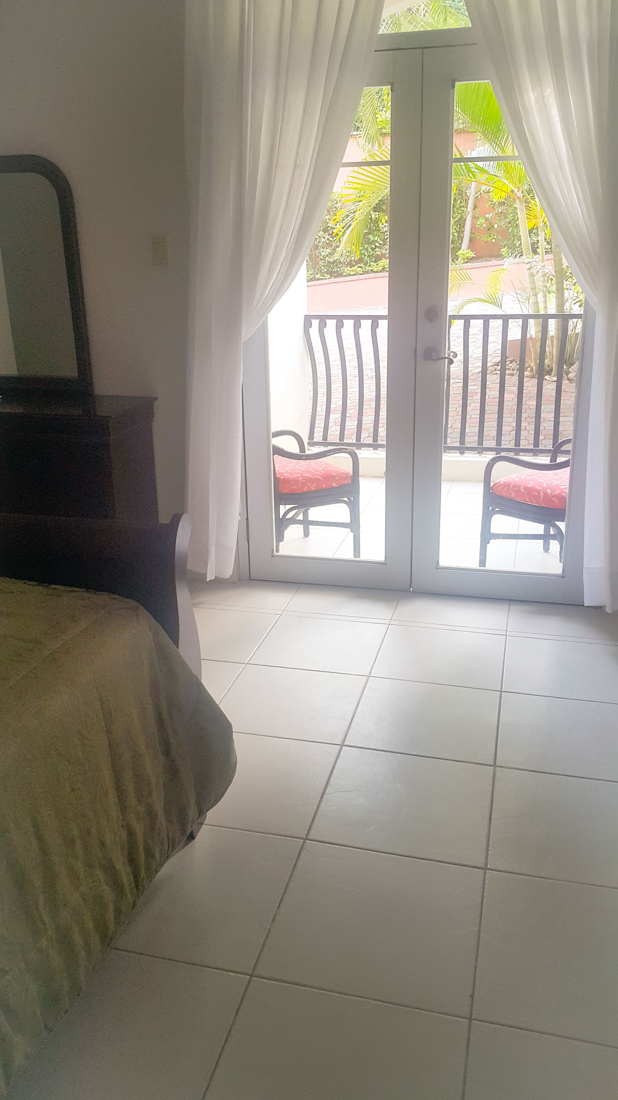 A room with a bed, a chair, and a view of a balcony with a railing and a chair.