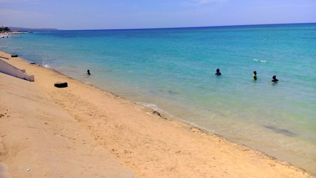 Una platja amb aigua turquesa cristal·lina, sorra daurada i algunes persones banyant-se.