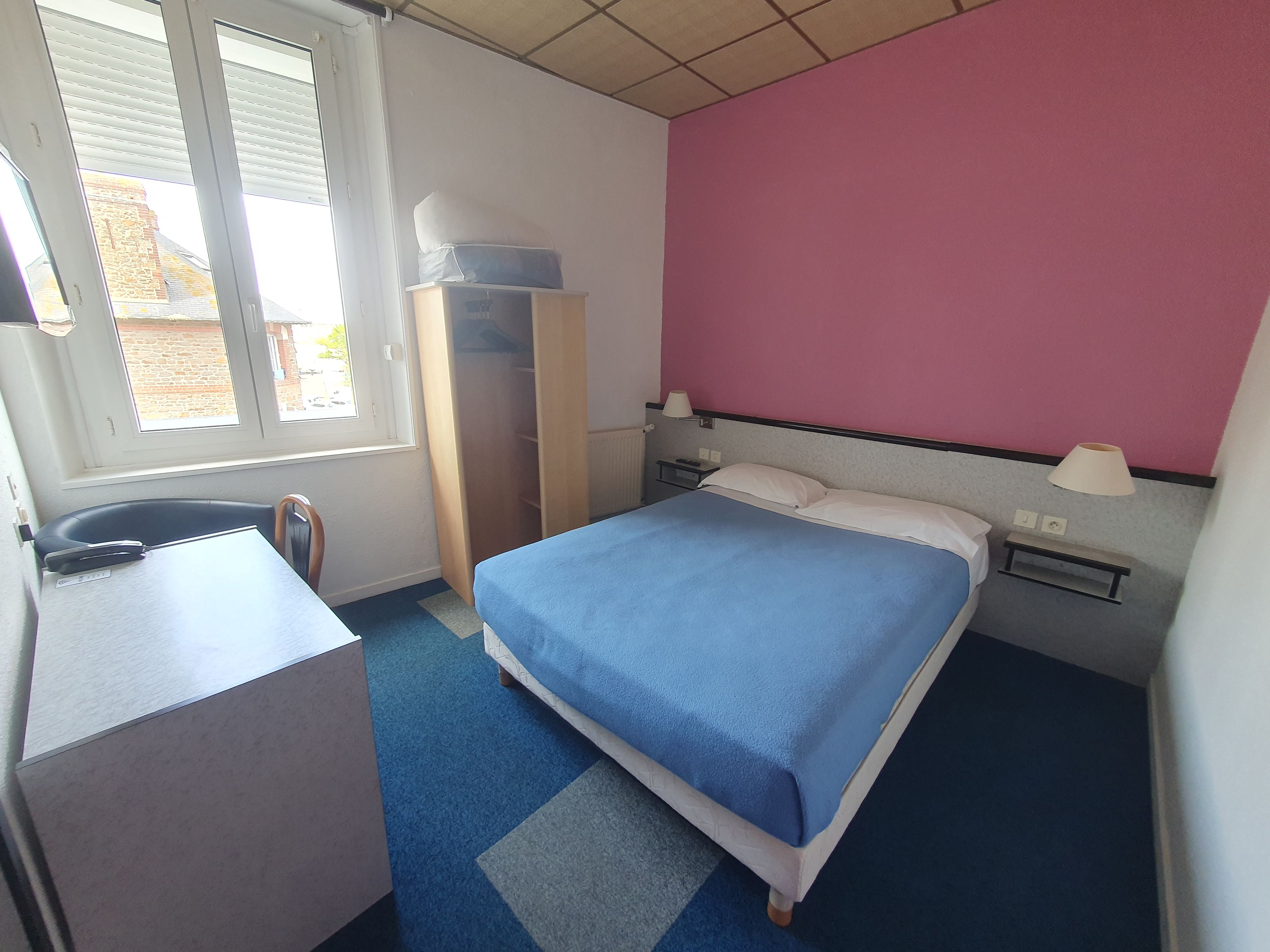 A hotel room with a bed, a desk, a chair, a wardrobe, and a window.