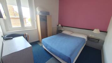 A hotel room with a bed, a desk, a chair, a wardrobe, and a window.