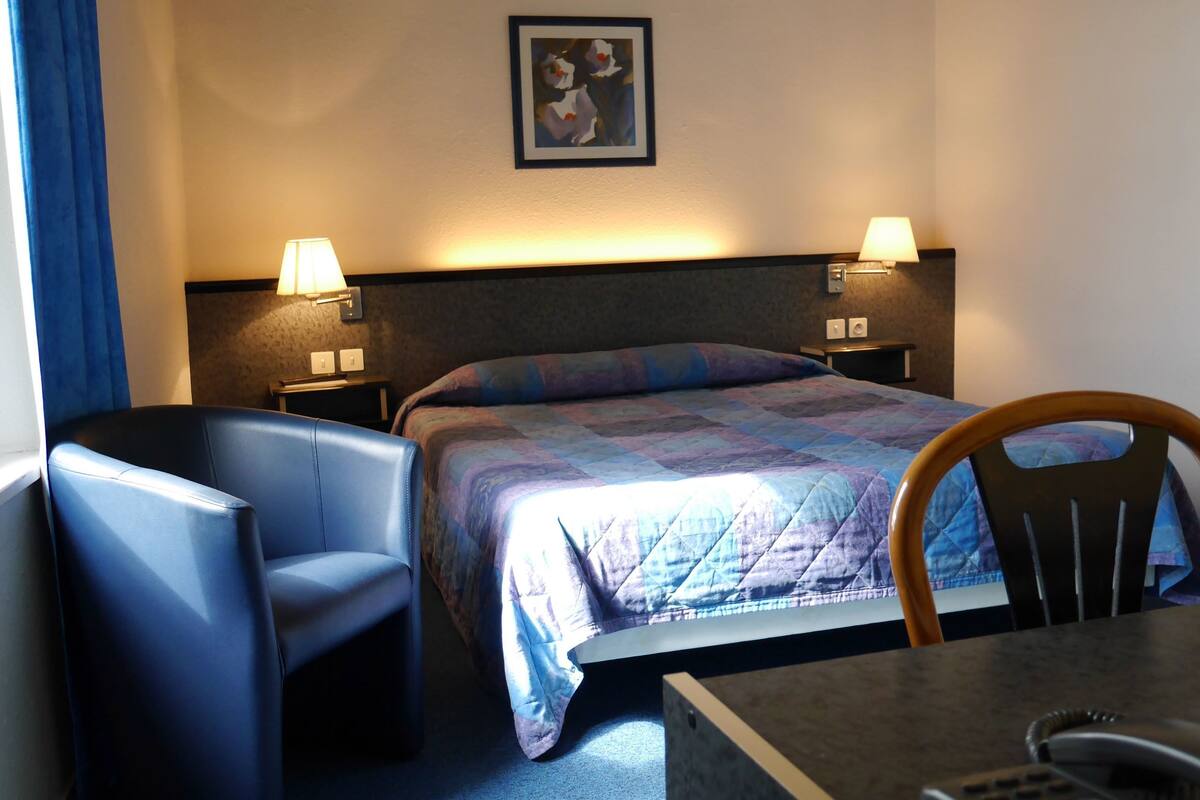 A hotel room with a bed, two bedside lamps, a chair, a desk, and a telephone.
