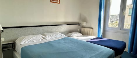 Une chambre d’hôtel avec deux lits, une fenêtre avec des rideaux, un radiateur et une lampe fixée au mur.