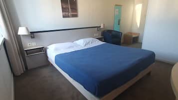 Een hotelkamer met een bed, nachtkastje, lamp, stoel en een deur.