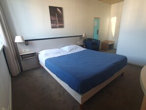 Una habitación de hotel con cama, mesita de noche, lámpara, silla y puerta.