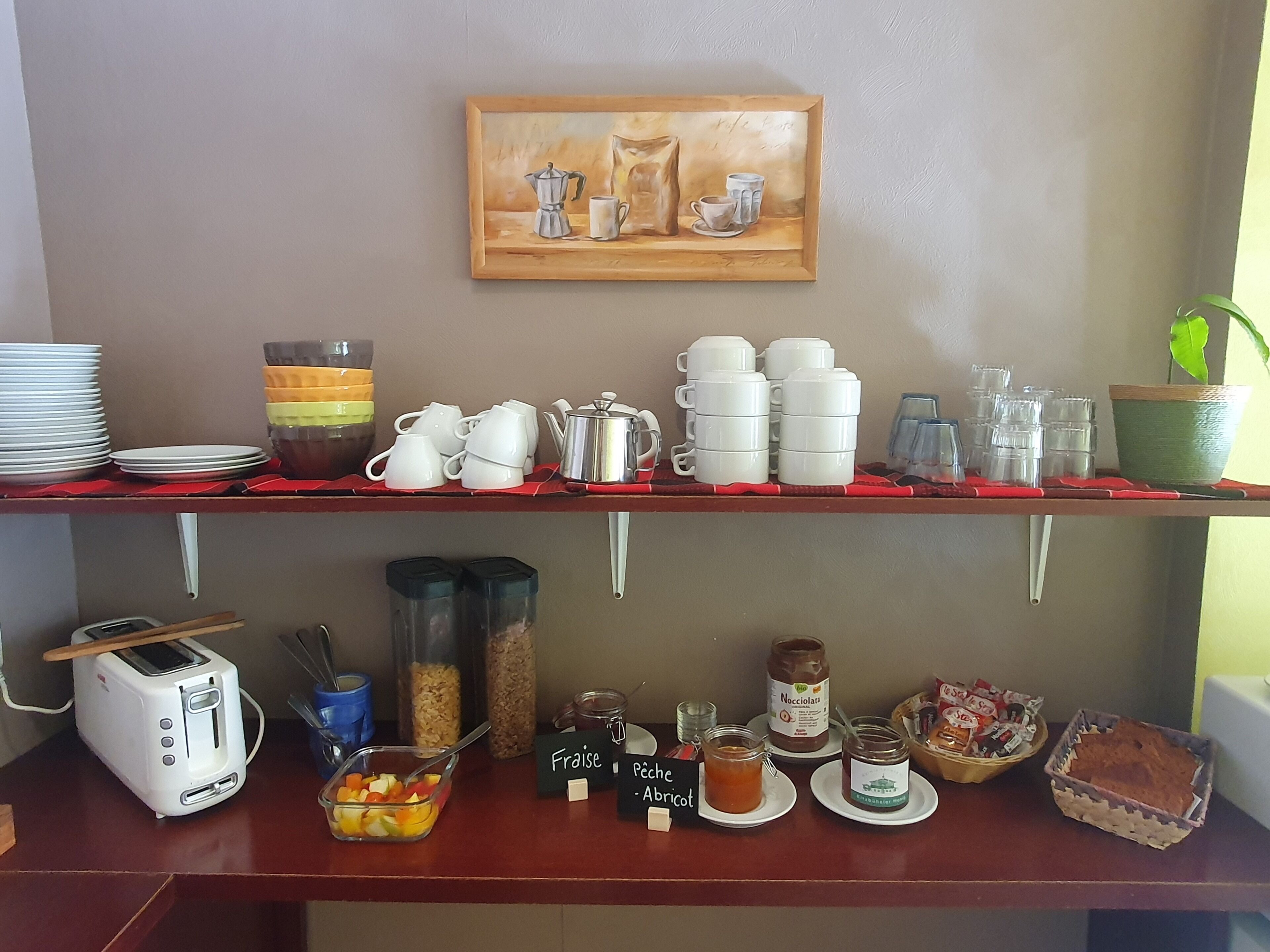 Een ontbijtbuffet met diverse etenswaren, bestek en een schilderij aan de muur.