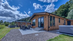 A wooden cabin with large windows and a patio area with outdoor seating. - Balloch Park (Aberfeldy)