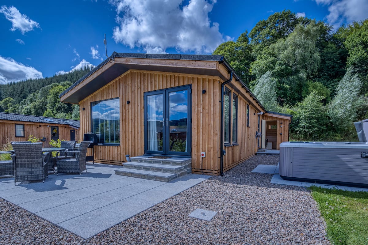 Una cabaña de madera con un área de patio, mobiliario exterior y un jacuzzi.