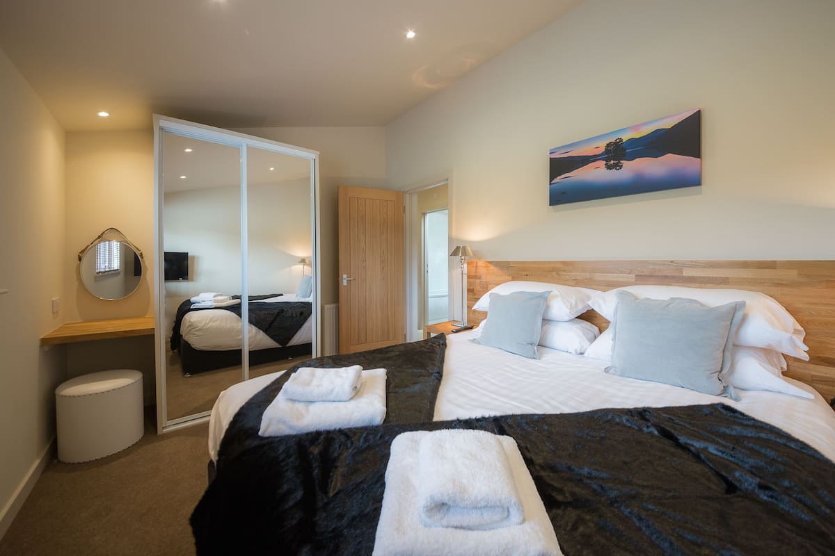 Un cuarto de hotel con una cama grande, cabecera de madera, un cuadro en la pared y un espejo.