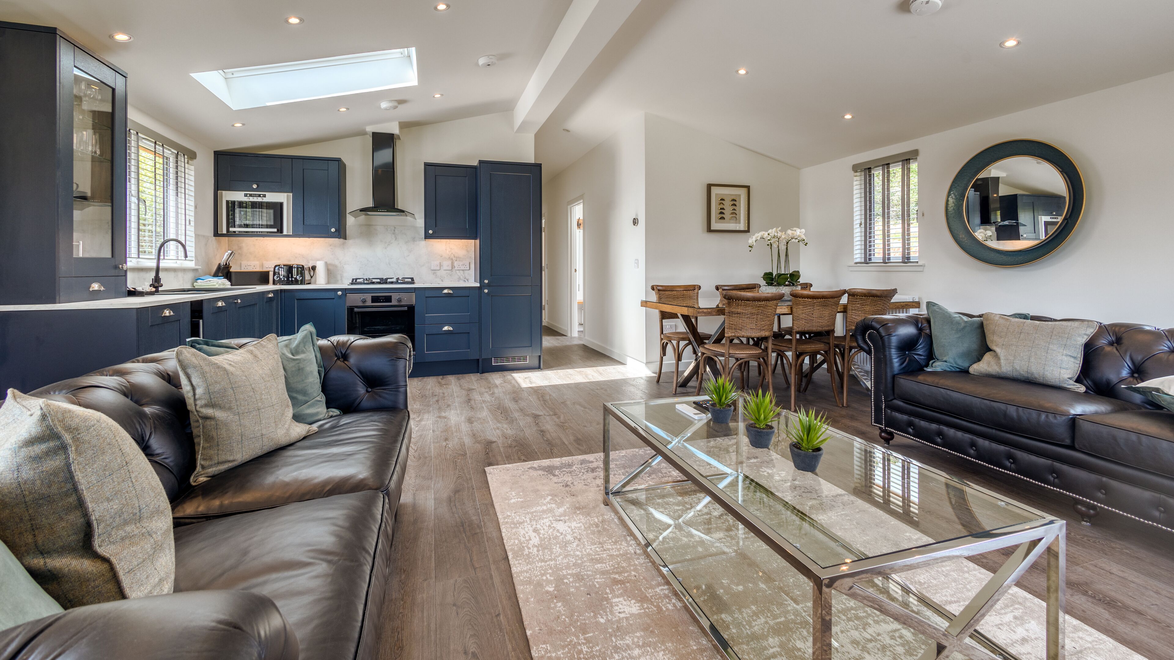 A modern living room with a leather sofa, a glass coffee table, and a dining area with wicker chairs.