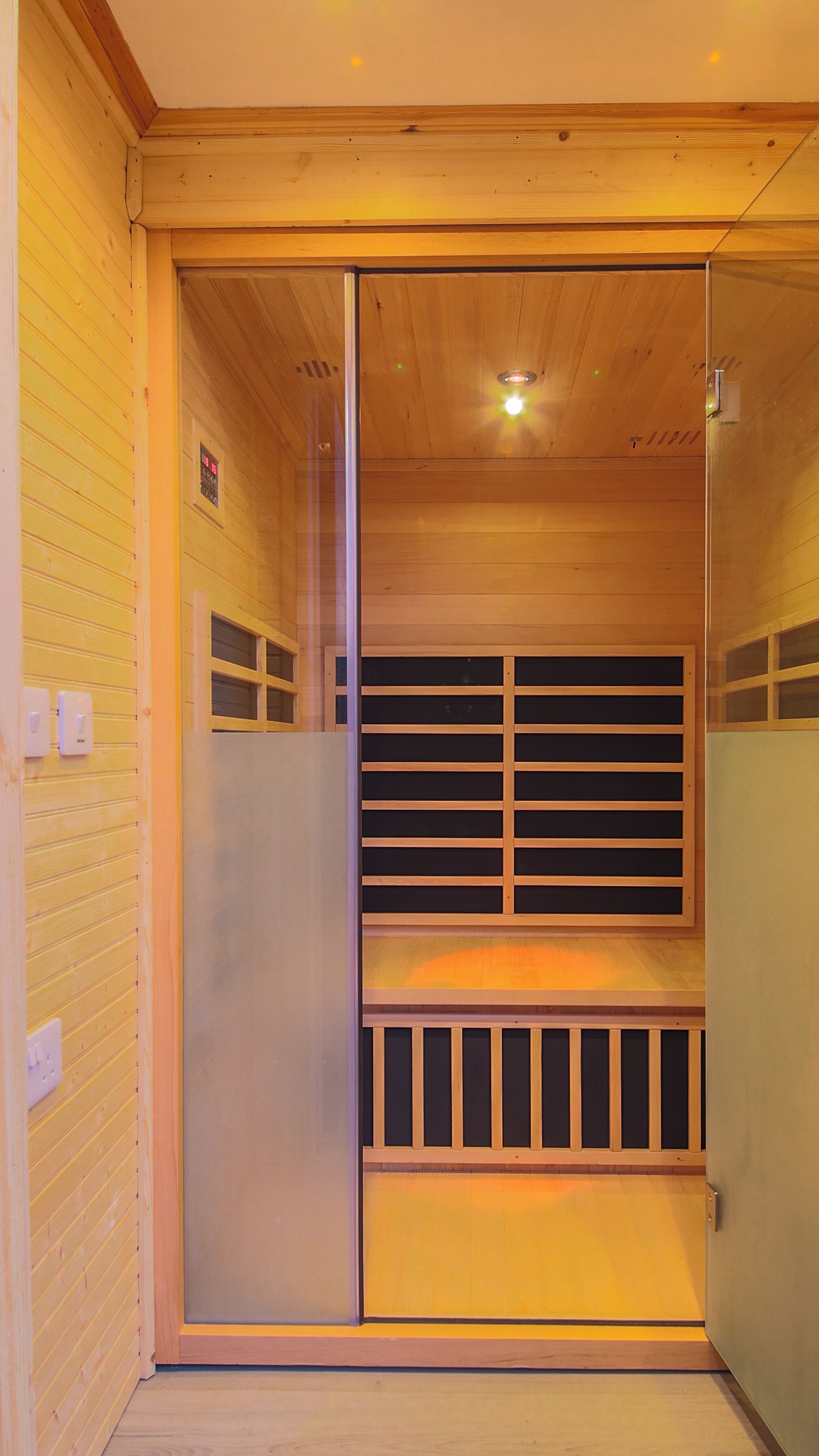 A sauna room with wooden walls and a glass door.