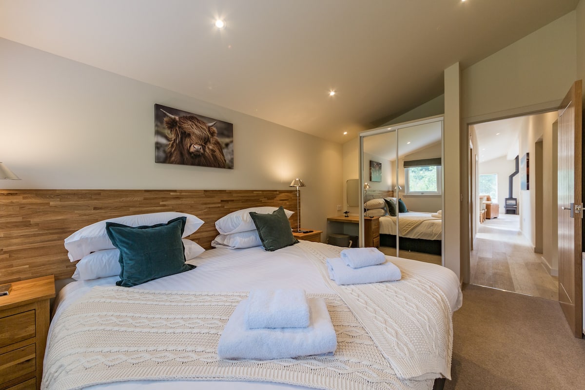 Una habitación de hotel moderna con una cama grande, un cabecero de madera y un espejo que refleja el espacio.