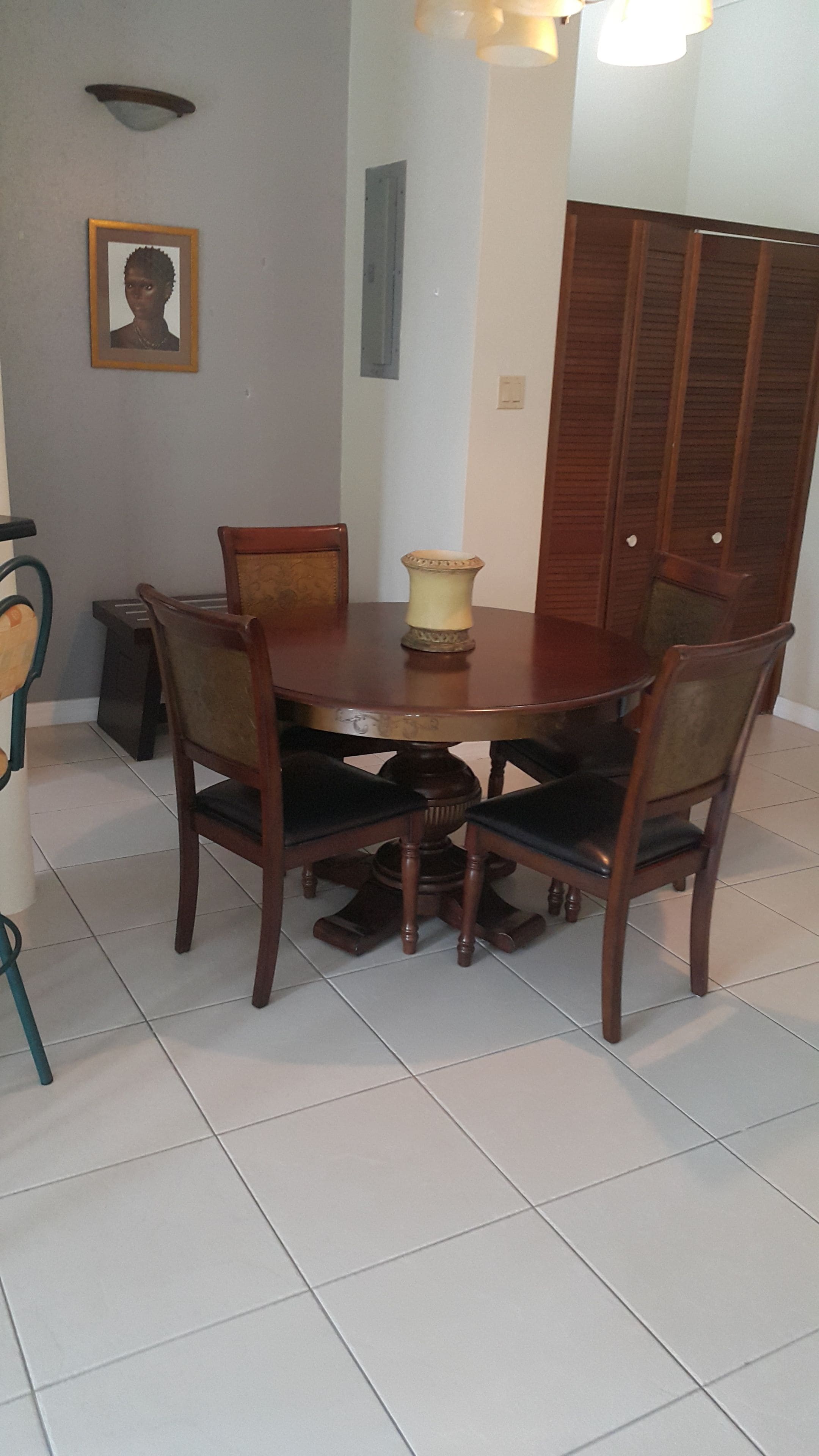 A dining area with a round wooden table, four chairs, a vase, and a framed picture on the wall.