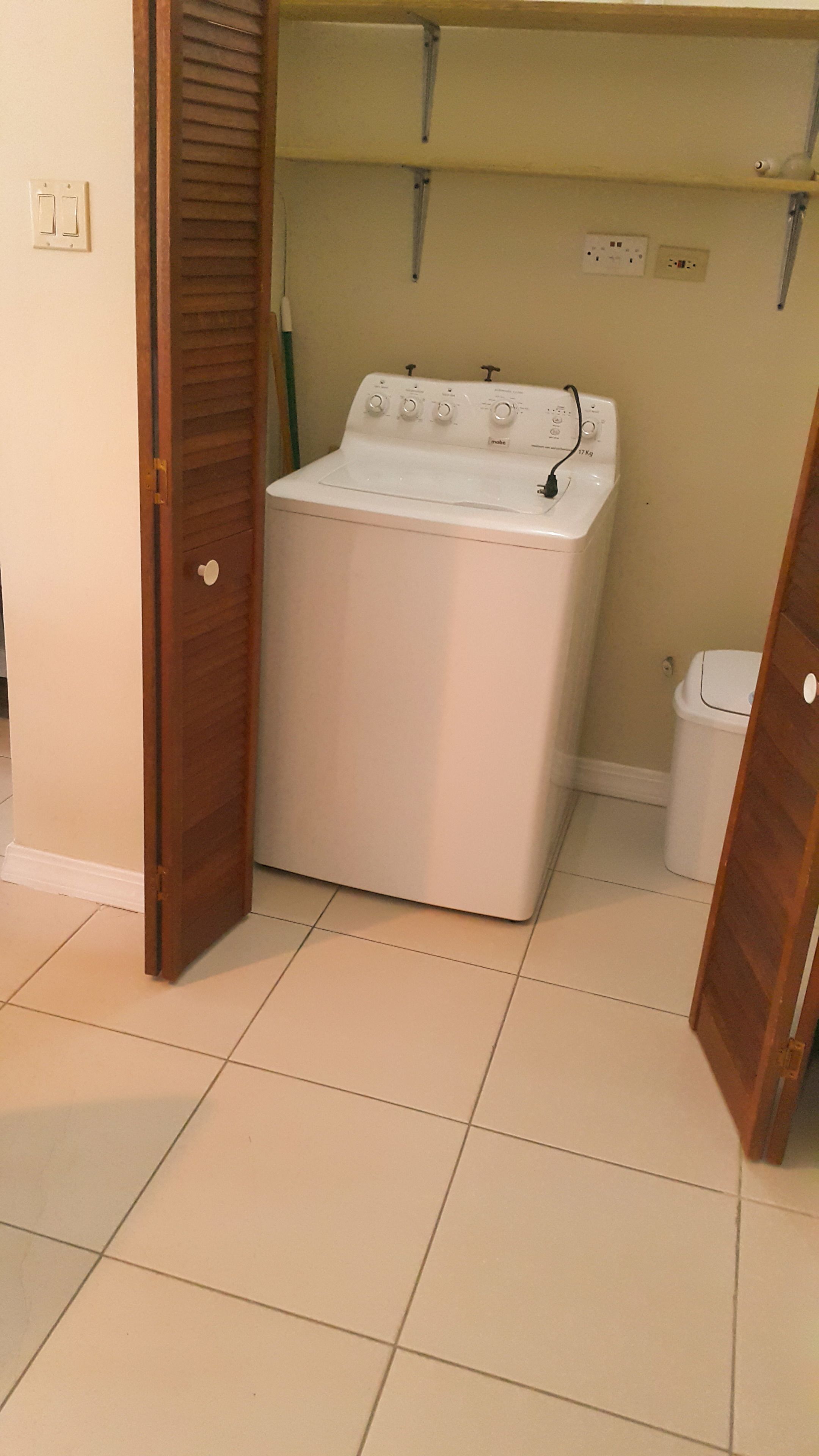 Une buanderie équipée d’un lave-linge et d’un sèche-linge à chargement frontal, de portes en bois et d’un revêtement de sol carrelé.