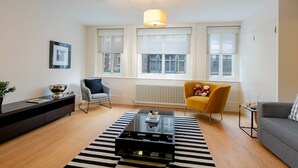 A modern living room with a glass coffee table, a sofa, a yellow armchair, and a black and white striped rug. - D'Arblay Street (London)