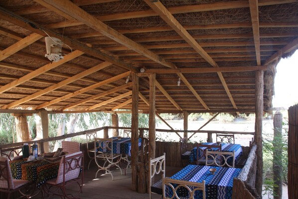 Un espacio de estar al aire libre cubierto, con vigas de madera y mesas con manteles estampados.