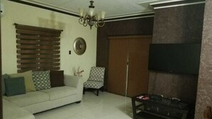 A living room with a sofa, a patterned armchair, a TV mounted on the wall, and a wooden cabinet. - The Hamptons of Acadia (Kingston)