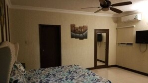 A bedroom with a bed, a ceiling fan, a door, a wall-mounted TV, and an air conditioning unit. - The Hamptons of Acadia (Kingston)