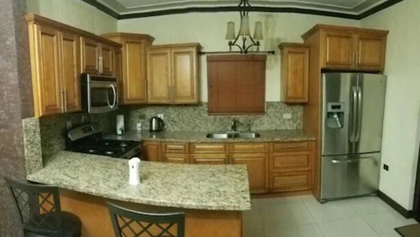 A kitchen with wooden cabinets, a granite countertop, a stainless steel refrigerator, and a built-in microwave. - The Hamptons of Acadia (Kingston)