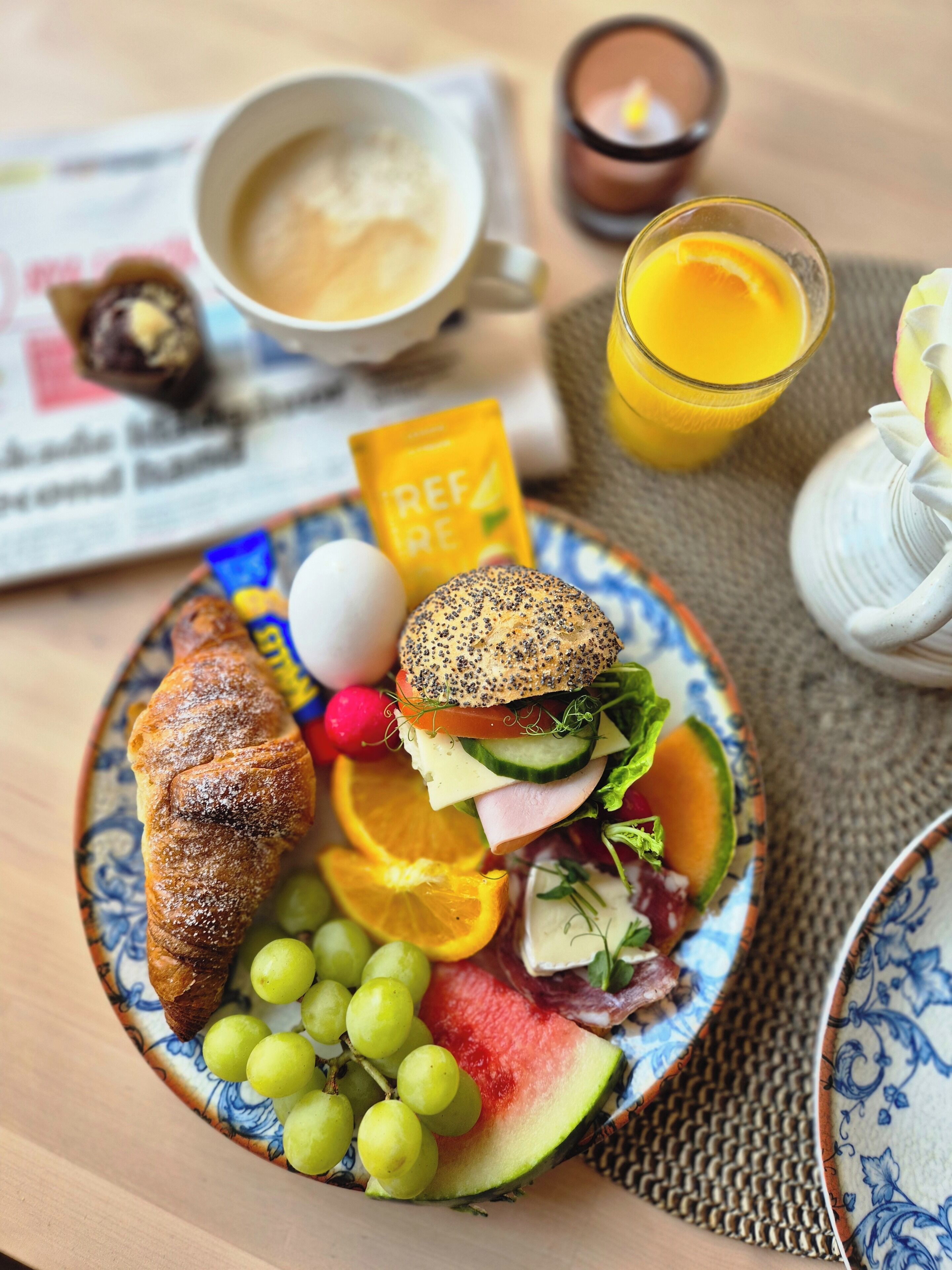 A breakfast plate with a croissant, a sandwich, grapes, watermelon, and a glass of orange juice.