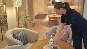 Una habitación de hotel con una mesa redonda de madera, dos sillones, una lámpara y una planta en maceta.