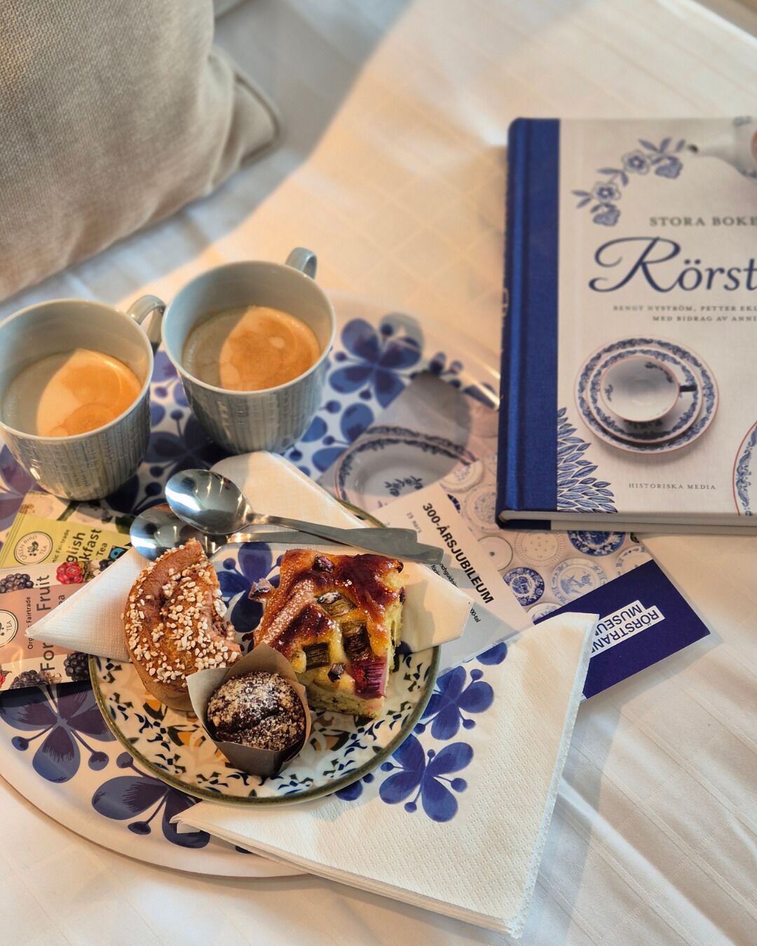 Ett bord med en tallrik mat, två koppar, en sked, en bok och en servett.