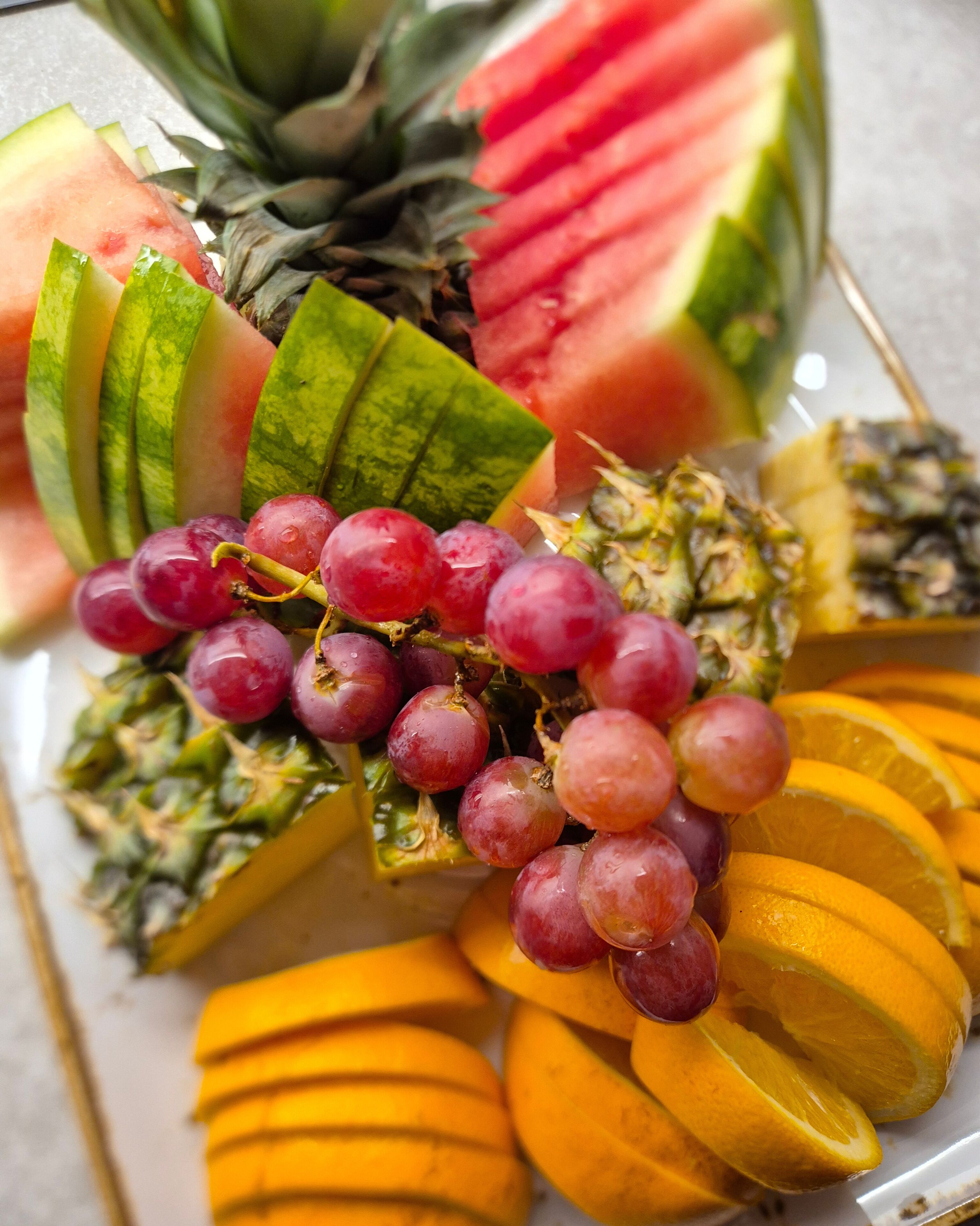 A fruit platter with watermelon, pineapple, grapes, mango slices, and orange segments.