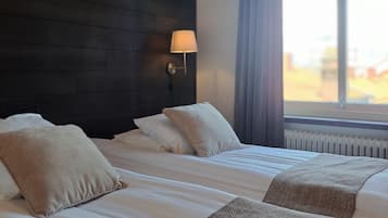 Habitación de hotel con dos camas, cabecera de madera oscura, lámpara de pared y un ventanal con cortinas.