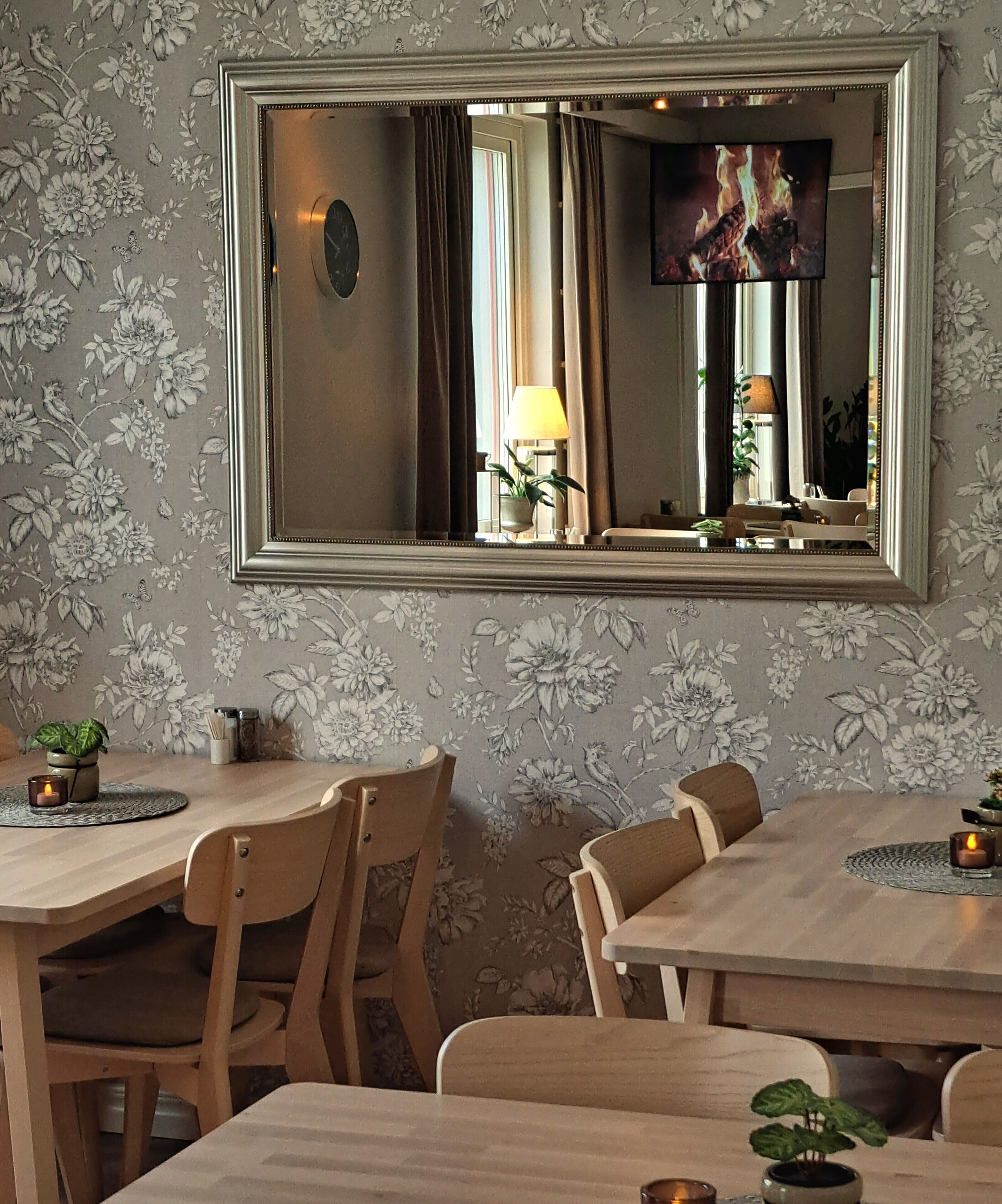 Comedor con un espejo grande, papel tapiz floral y muebles de madera.