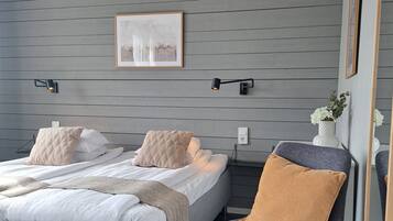 A modern bedroom with two beds, a gray wall, a framed abstract painting, and a side table with a vase.
